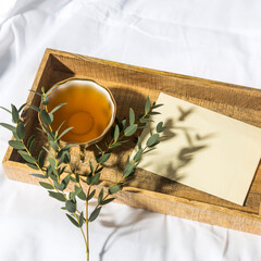 A eucalyptus branch lies on a white sheet beside a tray with a cup of tea and a saucer in a letter in an envelope. The garland is glowing.