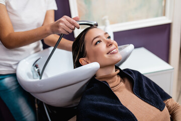 Professional hairdresser washing hair of a beautiful young adult woman in hair salon.