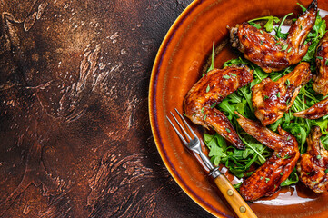 Baked chicken wings with sweet chili sauce on a plate with arugula. Dark background. Top view. Copy space