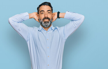 Middle aged man with beard wearing business shirt relaxing and stretching, arms and hands behind head and neck smiling happy