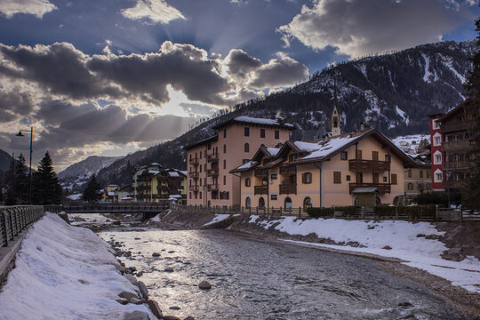 Houses and hotels in Moena, a city in italian Val di Fassa on a sunny winter day rising over the river in the centre