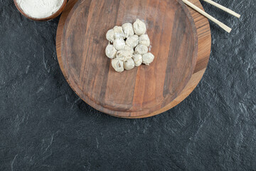 A wooden round board with uncooked dumplings and flour