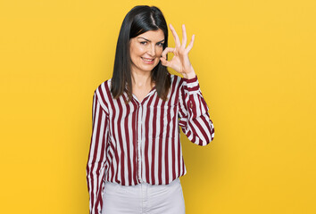 Beautiful brunette woman wearing striped shirt smiling positive doing ok sign with hand and fingers. successful expression.
