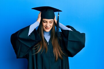 Beautiful brunette young woman wearing graduation cap and ceremony robe suffering from headache desperate and stressed because pain and migraine. hands on head.