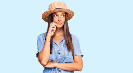 Obraz na płótnie Canvas Young hispanic woman wearing summer hat serious face thinking about question with hand on chin, thoughtful about confusing idea