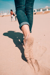 Beach travel - woman in a jeanse walking on sand beach leaving footprints in the sand. Closeup detail of female feet and sand on Holland coast, North Sea