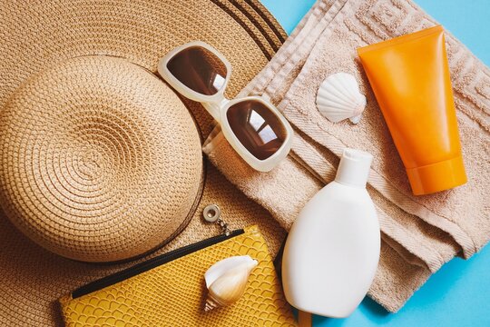 Flat lay summer travel image. View from above beach essentials. Straw hat, moisturizing sunscreen for sensitive skin and body lotion, sunglasses and cosmetic bag