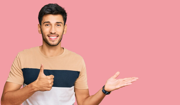 Young handsome man wearing casual clothes showing palm hand and doing ok gesture with thumbs up, smiling happy and cheerful
