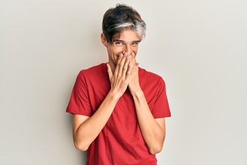 Young hispanic man wearing casual clothes laughing and embarrassed giggle covering mouth with...