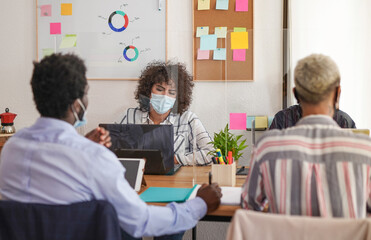 Young multiracial people working in office with dividers and face masks for coronavirus outbreak