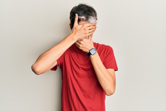 Young hispanic man wearing casual clothes covering eyes and mouth with hands, surprised and shocked. hiding emotion