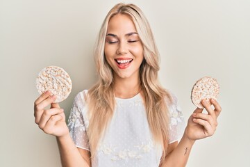 Beautiful caucasian blonde girl eating healthy rice crackers smiling and laughing hard out loud...