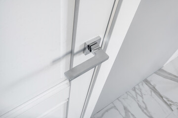 Modern metal door handle on white wooden door in interior. Knob close-up elements. Door handle, fittings for interior design