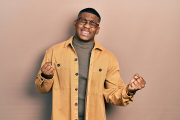 Young black man wearing casual clothes and glasses very happy and excited doing winner gesture with arms raised, smiling and screaming for success. celebration concept.
