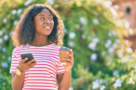 Young african american girl using smartphone drinking coffee at the park.