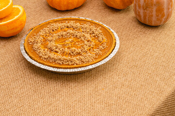 Fresh baked homemade pumpkin pie decorated with crushed nuts and orange zest close up on kitchen table on rustic background