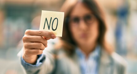 Young hispanic businesswoman with serious expression holding reminder with no message at the city.
