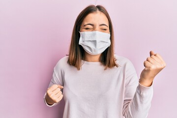 Young beautiful woman wearing medical mask celebrating surprised and amazed for success with arms raised and eyes closed