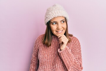 Young beautiful woman wearing wool sweater and winter hat smiling looking confident at the camera with crossed arms and hand on chin. thinking positive.