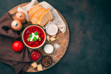 Beetroot soup with sour cream and basil, bread, tomato and tomato sauce on a wooden round board on a concrete brown background.