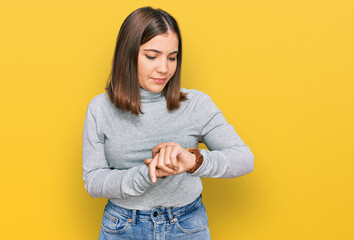 Young beautiful woman wearing casual turtleneck sweater checking the time on wrist watch, relaxed...