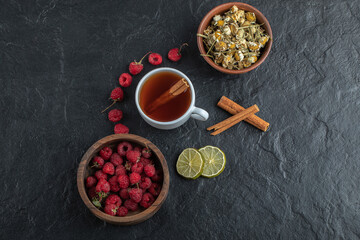 Fototapeta na wymiar Cup of tea with fresh raspberries and chamomile on black background