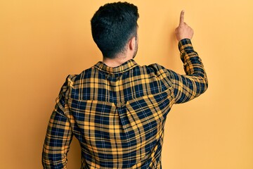 Young hispanic man wearing casual clothes posing backwards pointing ahead with finger hand