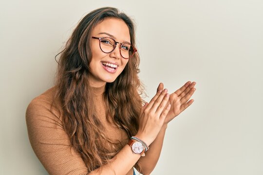 Young hispanic girl wearing casual clothes and glasses clapping and applauding happy and joyful, smiling proud hands together
