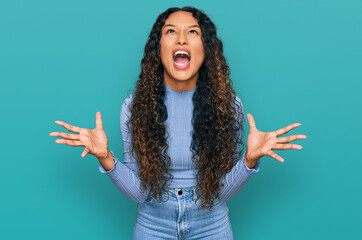 Young hispanic woman with curly hair wearing casual clothes crazy and mad shouting and yelling with...