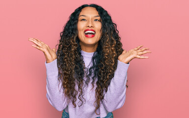 Young hispanic woman with curly hair wearing casual winter sweater celebrating mad and crazy for success with arms raised and closed eyes screaming excited. winner concept