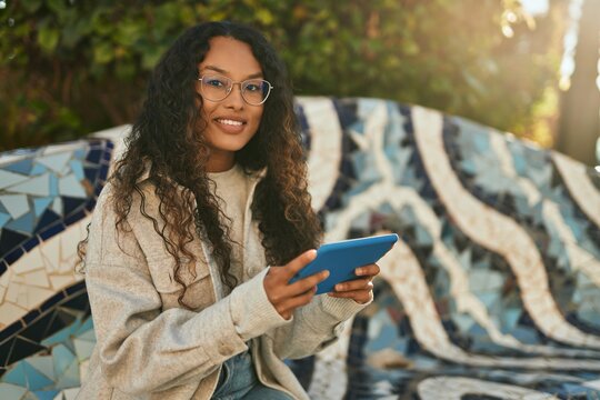 Young latin woman smiling happy using touchpad sitting on the bench at the city.