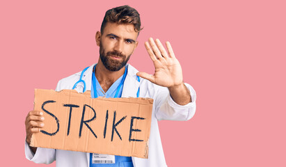 Young hispanic man wearing doctor stethoscope holding strike banner with open hand doing stop sign with serious and confident expression, defense gesture