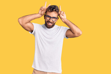 Fototapeta na wymiar Young hispanic man wearing casual clothes and glasses posing funny and crazy with fingers on head as bunny ears, smiling cheerful