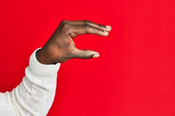 Arm and hand of african american black young man over red isolated background picking and taking invisible thing, holding object with fingers showing space