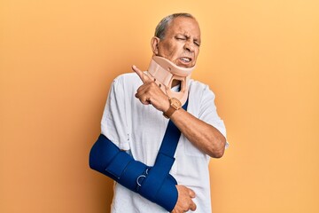Handsome mature senior man wearing cervical collar and arm on sling pointing aside worried and...