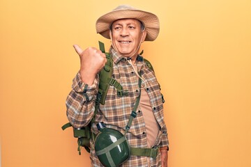 Fototapeta premium Senior man with grey hair wearing hiker backpack and water canteen pointing thumb up to the side smiling happy with open mouth