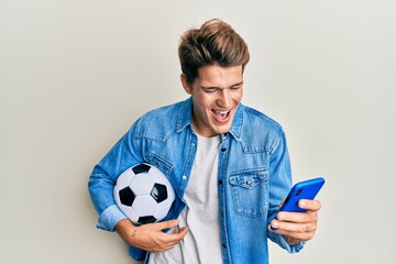 Handsome caucasian man holding football ball looking at smartphone smiling and laughing hard out loud because funny crazy joke.