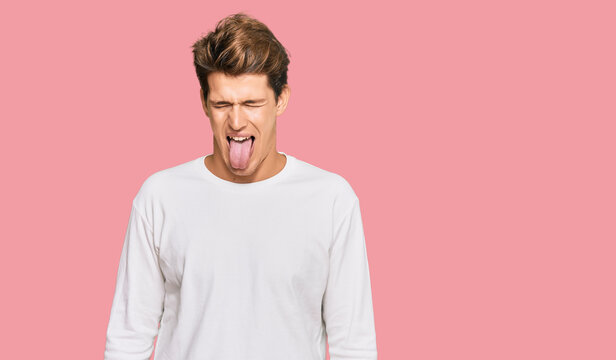 Handsome caucasian man wearing casual white sweater sticking tongue out happy with funny expression. emotion concept.
