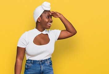 Young african woman with turban wearing hair turban over isolated background very happy and smiling looking far away with hand over head. searching concept.