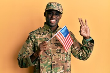 Young african american man wearing army uniform holding american flag doing ok sign with fingers, smiling friendly gesturing excellent symbol