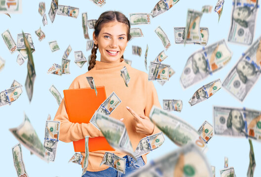 Beautiful caucasian woman with blonde hair holding book smiling happy pointing with hand and finger