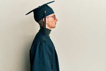 Young caucasian man wearing graduation cap and ceremony robe looking to side, relax profile pose...