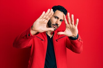 Young hispanic man wearing red leather jacket doing frame using hands palms and fingers, camera perspective