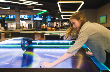 Tween girl plays air hockey in the entertainment center.