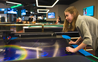 Tween girl plays air hockey in the entertainment center.