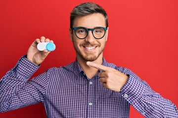 Handsome caucasian man wearing glasses and holding contact lenses smiling happy pointing with hand...