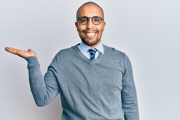 Hispanic adult man wearing glasses and business style smiling cheerful presenting and pointing with palm of hand looking at the camera.
