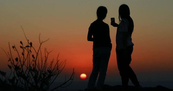 silhouette friend taking pictures of sunset with her smartphone