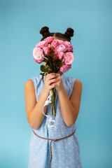 little child girl holding bouquet of roses in front of her face on blue studio background.