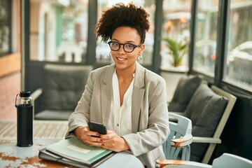 Young african american businesswoman smiling happy using smartphone sitting at coffee shop.